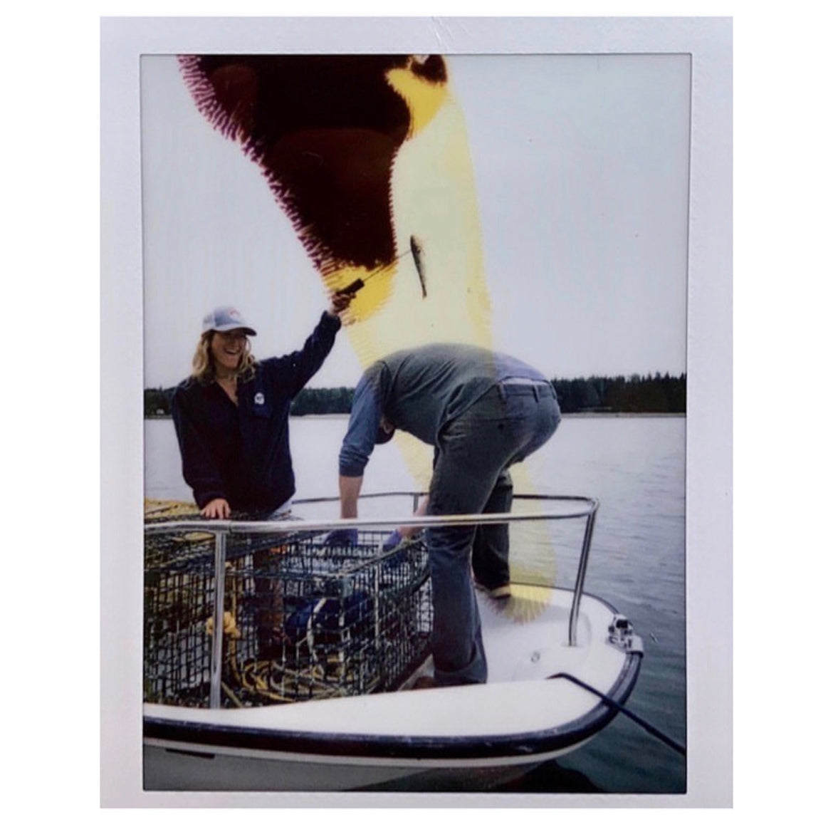 Instant photo of Brooke and Evan on a lobster boat, Brooke smiling and holding up bait while Evan works the traps