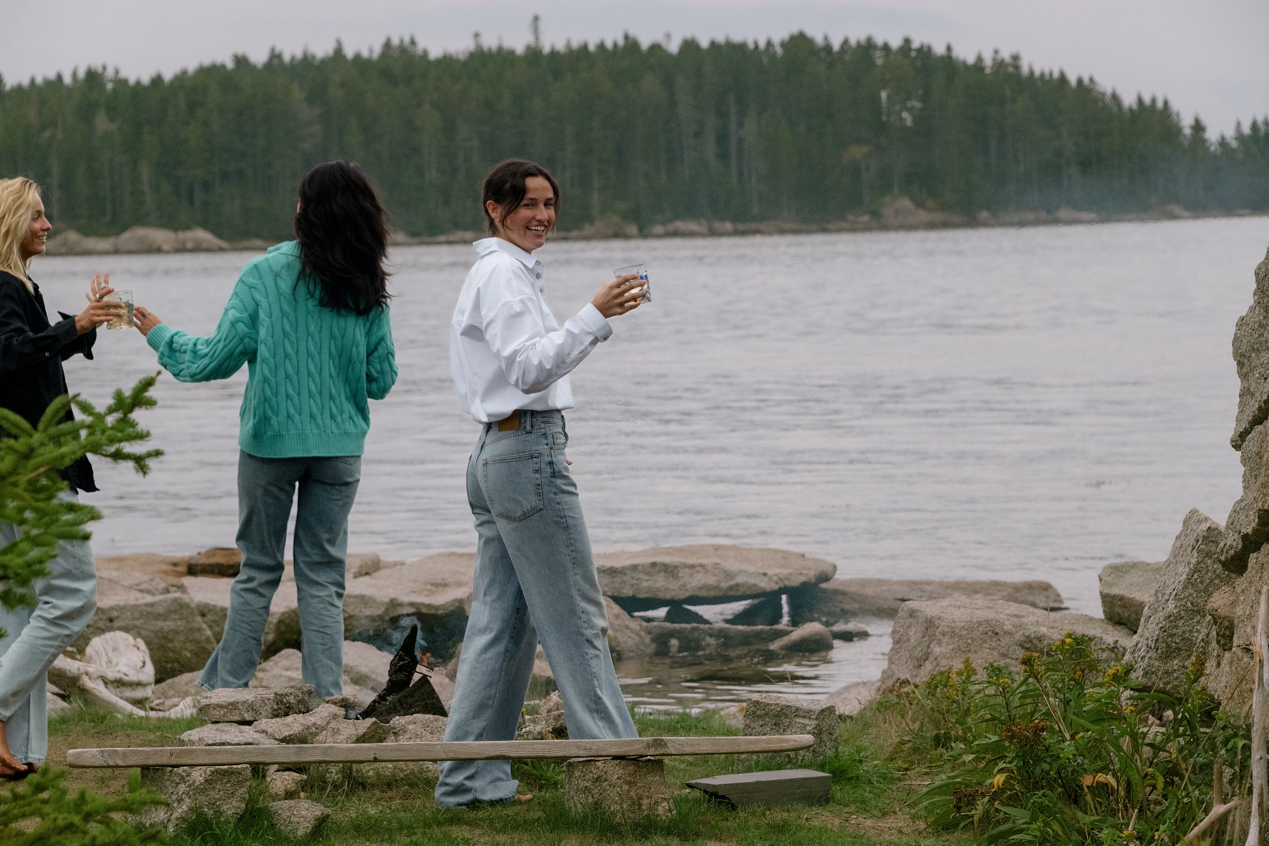 Three friends sharing drinks on the rocks by the water, one in the white Darty Popover