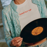 Close-up of the Going Out Top, white cropped tee with orange embroidered lettering, under a turquoise lace shirt with jeans