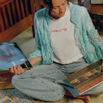 Model sitting cross-legged on the floor looking through records, wearing the Going Out Top with a lace shirt and jeans
