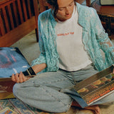 Model sitting cross-legged on the floor looking through records, wearing the Going Out Top with a lace shirt and jeans