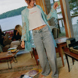 Model standing in a lakeside living room wearing the Going Out Top with a turquoise lace shirt and light-wash jeans